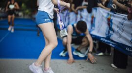 Runners cross the finish line at a marathon event in a city park. Participants rejoice and celebrate their achievements while others show signs of fatigue after the race.