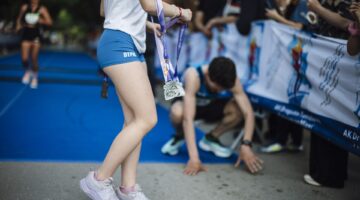 Runners cross the finish line at a marathon event in a city park. Participants rejoice and celebrate their achievements while others show signs of fatigue after the race.