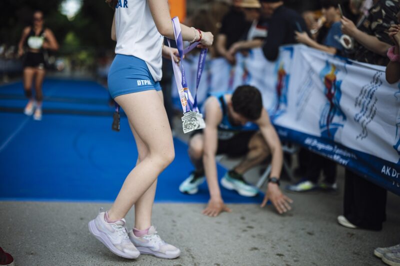 Runners cross the finish line at a marathon event in a city park. Participants rejoice and celebrate their achievements while others show signs of fatigue after the race.